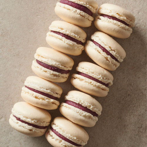 White chocolate and blackcurrant macarons stacked on a kitchen counter