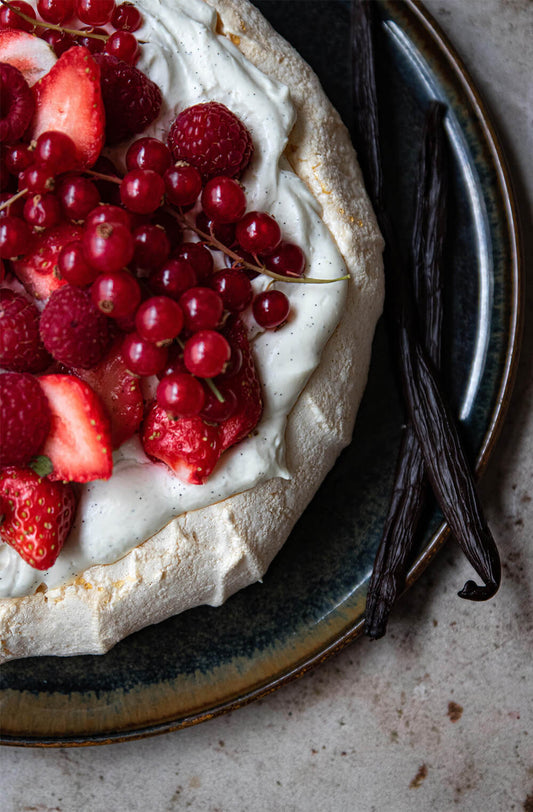 Pavlova with vanilla cream and fresh berries presented on a plate with vanilla beans on the side