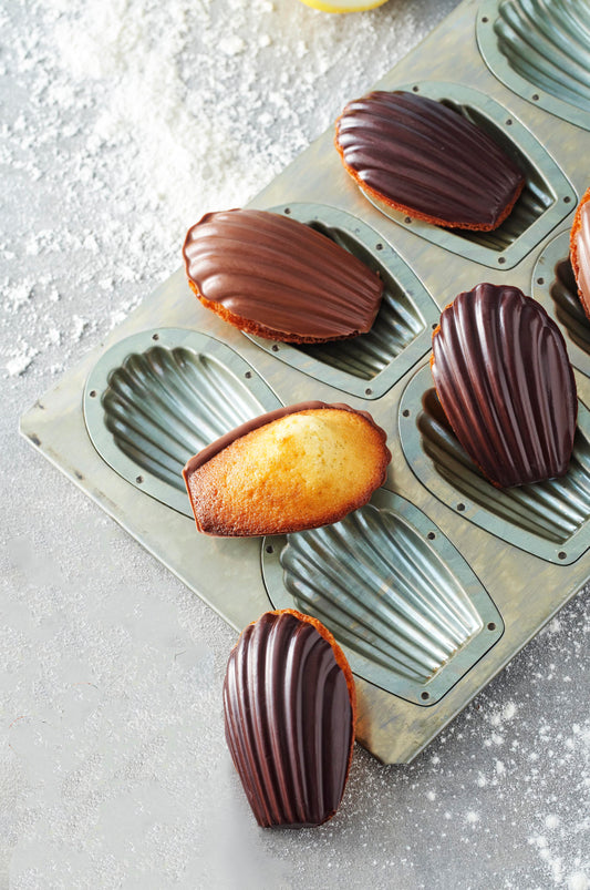 Dark chocolate glazed madeleines in their molds on a kitchen counter