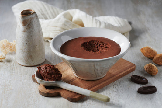 Dark chocolate plant-based mousse in a bowl with a spoon and pieces of chocolate and almond