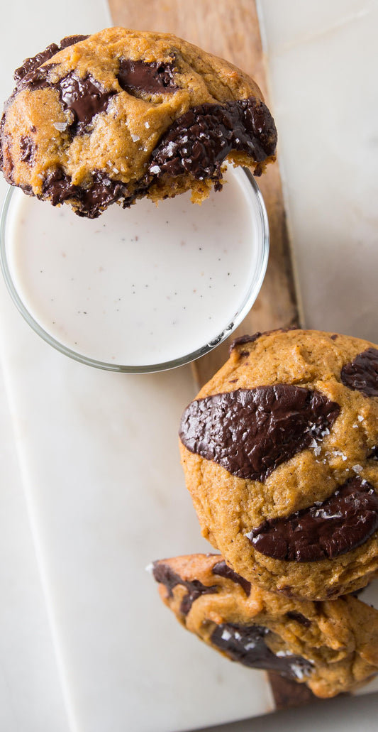 Dark chocolate chip pumpkin cookies on a plate with a glass of homemade vanilla milk 