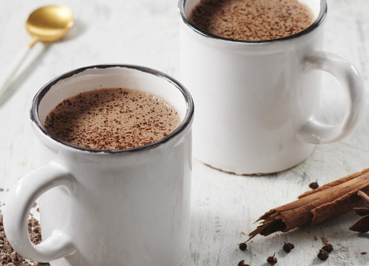 Hot chocolate with spices in two mugs with ground chocolate, cinnamon and star anise on the side